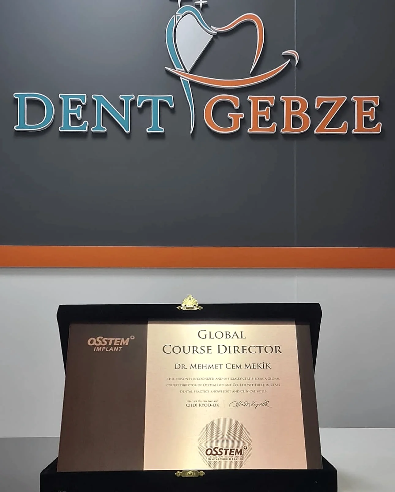 DENT GEBZE tabelasının önünde, kutusunda sergilenen bir 'Global Course Director' sertifika plaketi